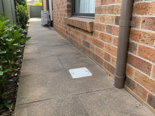 Outdoor paved side path with a drain cover beside a brick wall and downpipe in Putney